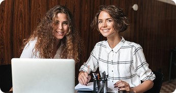 two smiling curly women working by table